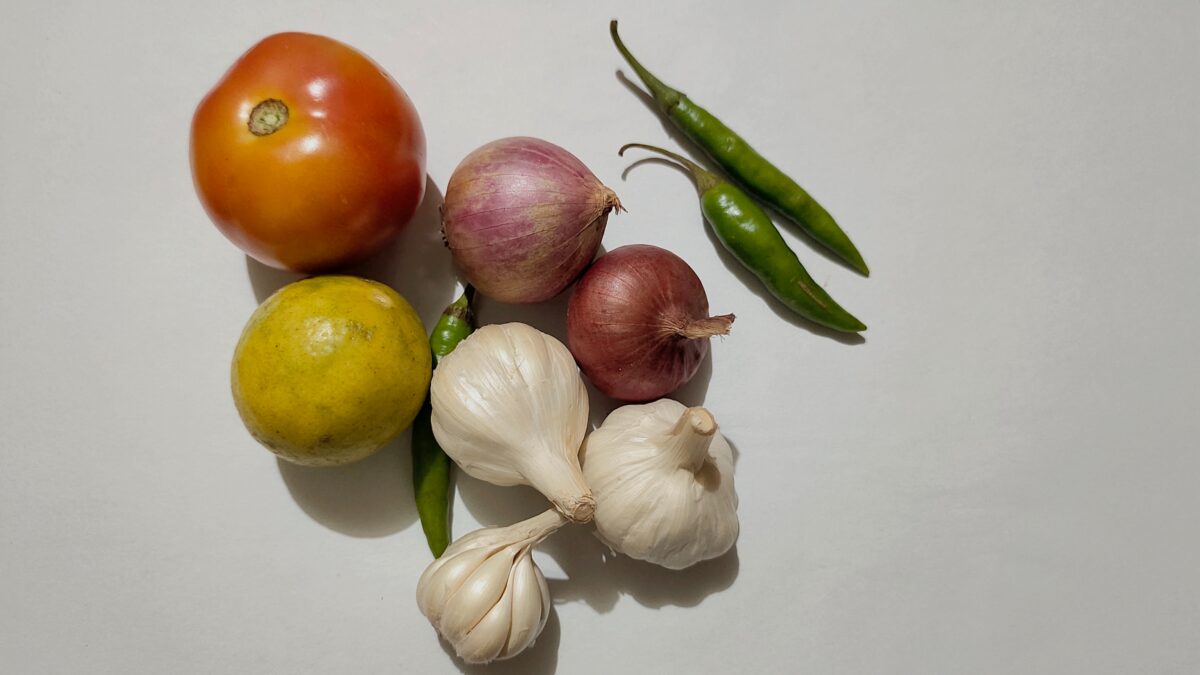 A selection of reduced vegetables including garlic, onions, a tomato and chili peppers.