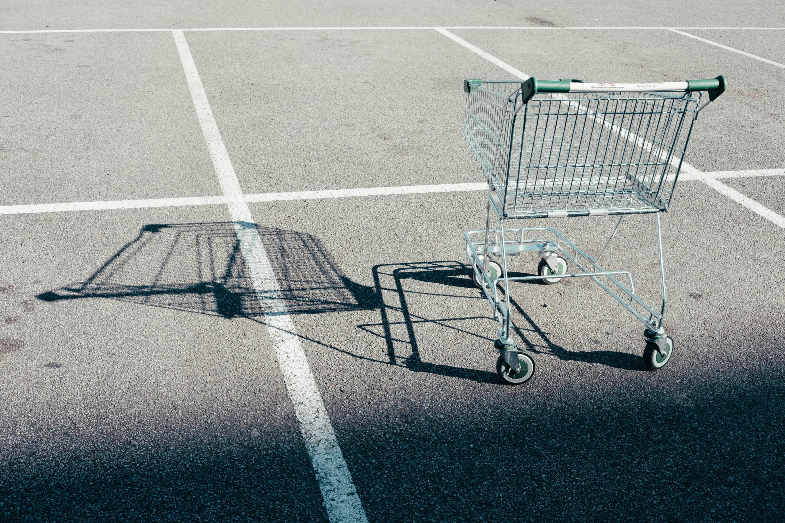 A decorative image of a supermarket trolley in a parking space of a car park, with the trolley casting a shadow over the ground.